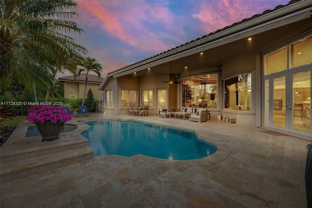 pool at dusk featuring a patio, ceiling fan, and french doors