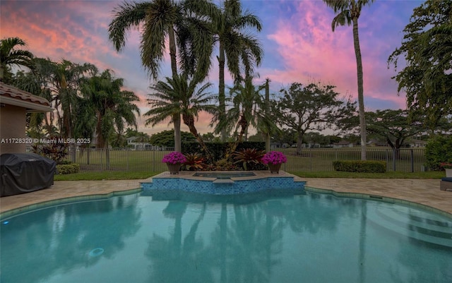 pool at dusk featuring an in ground hot tub, a grill, and a patio