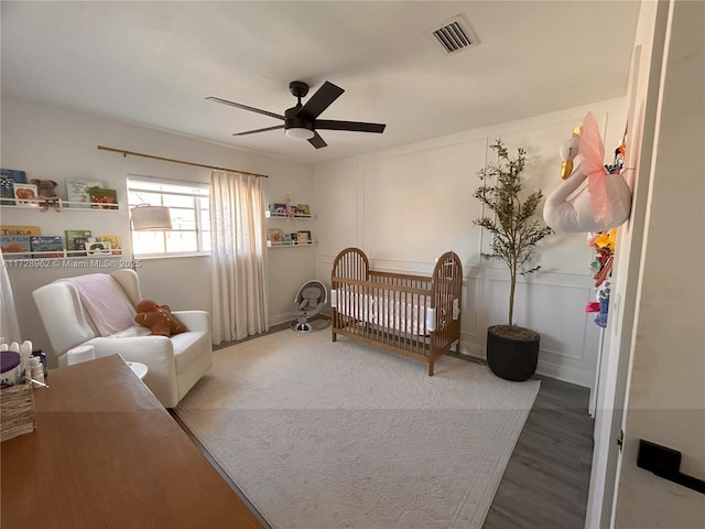 bedroom with ceiling fan, a nursery area, and hardwood / wood-style flooring