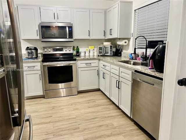 kitchen with light wood-type flooring, white cabinets, sink, stainless steel appliances, and light stone counters