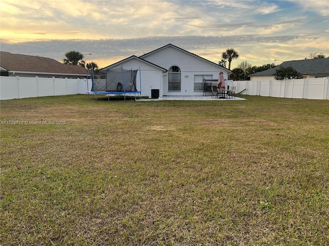 back house at dusk with a patio, a yard, and a trampoline