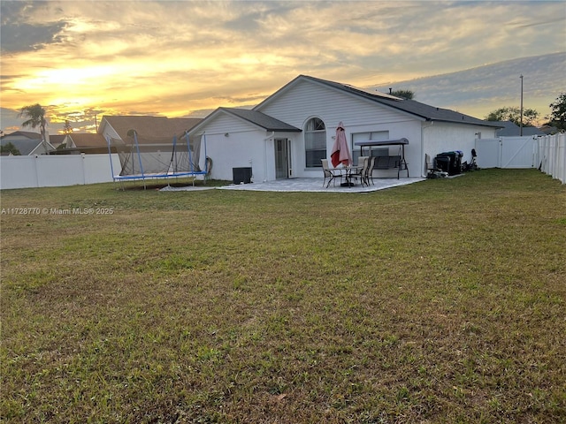 back house at dusk featuring central air condition unit, a trampoline, a lawn, and a patio area