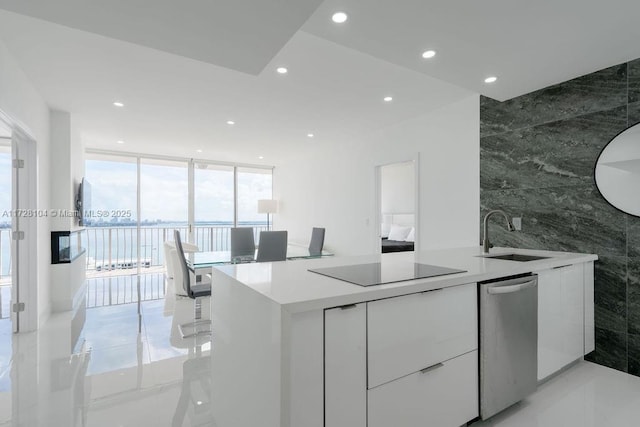 kitchen featuring black electric stovetop, floor to ceiling windows, stainless steel dishwasher, sink, and white cabinets