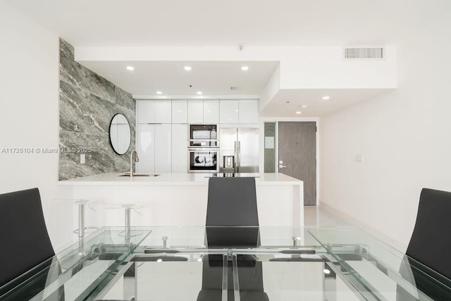 kitchen featuring sink, stainless steel fridge with ice dispenser, black microwave, and white cabinetry