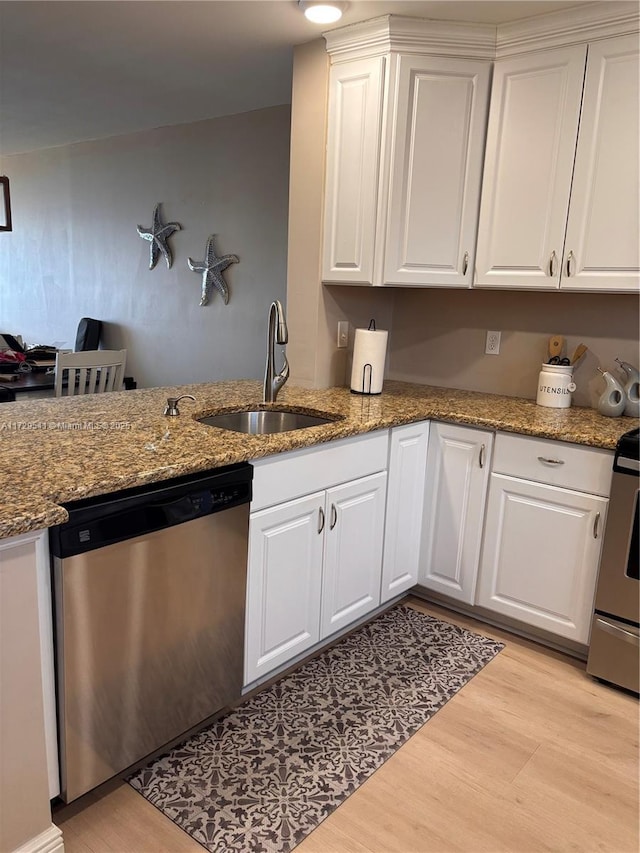 kitchen with appliances with stainless steel finishes, white cabinetry, sink, light wood-type flooring, and stone counters