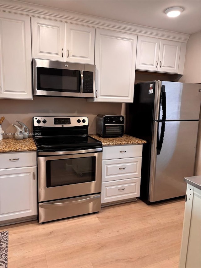 kitchen with light hardwood / wood-style floors, white cabinetry, appliances with stainless steel finishes, and dark stone countertops