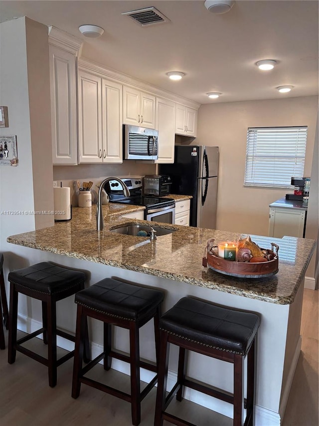 kitchen with appliances with stainless steel finishes, a kitchen bar, white cabinetry, light hardwood / wood-style floors, and kitchen peninsula