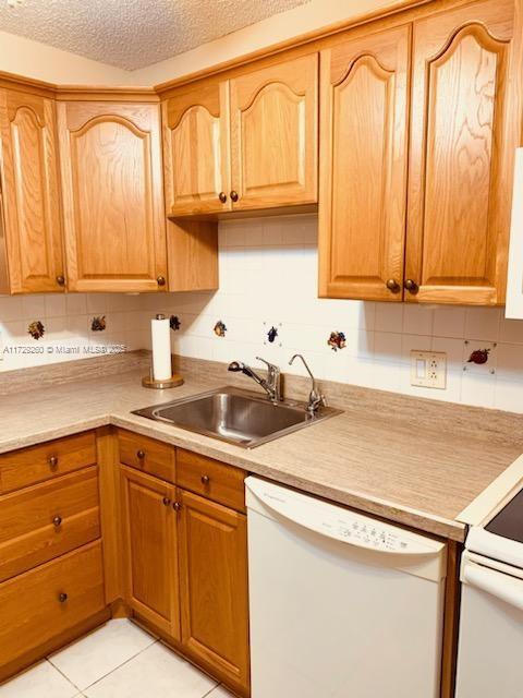 kitchen featuring dishwasher, decorative backsplash, sink, a textured ceiling, and light tile patterned floors