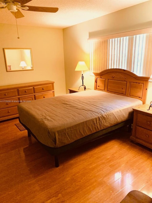 bedroom with light wood-type flooring, ceiling fan, and a textured ceiling