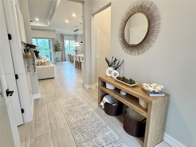 hallway with crown molding, light tile patterned flooring, and a tray ceiling