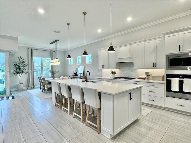 kitchen with custom exhaust hood, white cabinets, sink, an island with sink, and stainless steel appliances