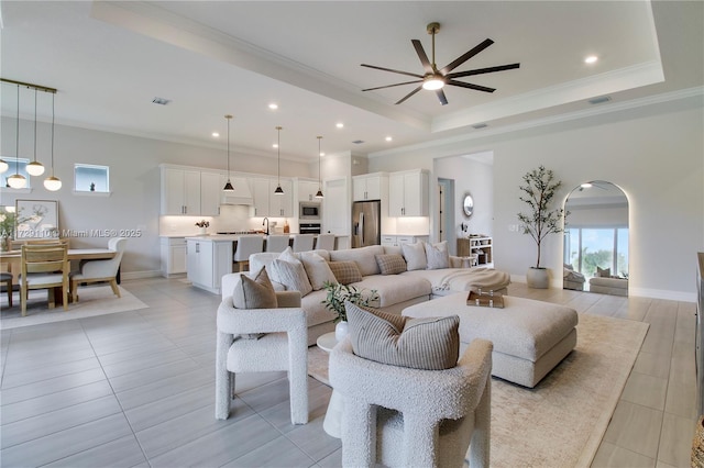 tiled living room with crown molding, ceiling fan, and a raised ceiling