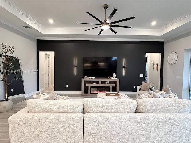 living room featuring ceiling fan, ornamental molding, and a tray ceiling