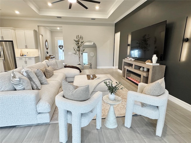 living room with ceiling fan, ornamental molding, a raised ceiling, and light wood-type flooring