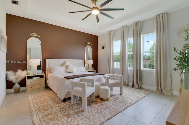 bedroom with a tray ceiling, light tile patterned flooring, and ceiling fan