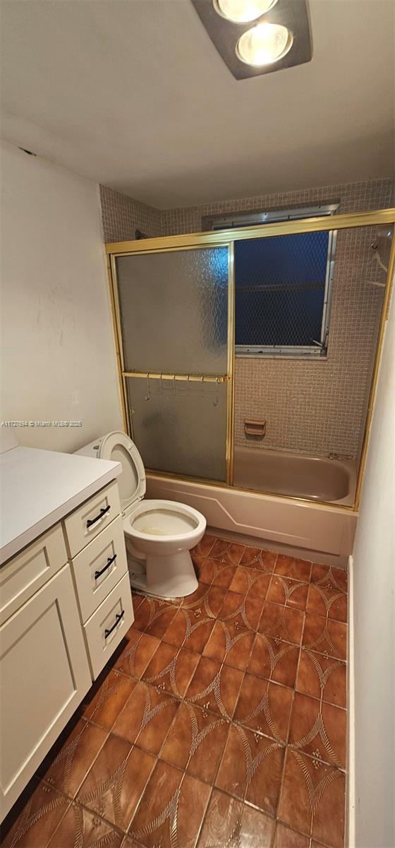 full bathroom with toilet, tile patterned floors, enclosed tub / shower combo, and vanity