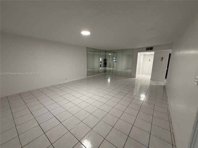 empty room with light tile patterned floors, visible vents, and a textured ceiling