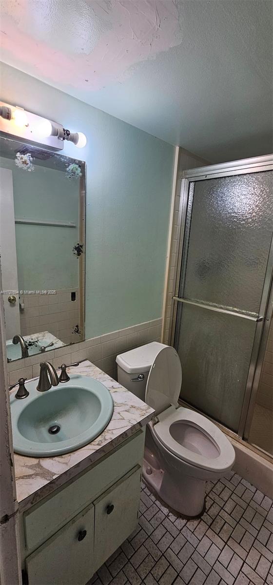 bathroom featuring toilet, tile walls, a shower with shower door, and vanity