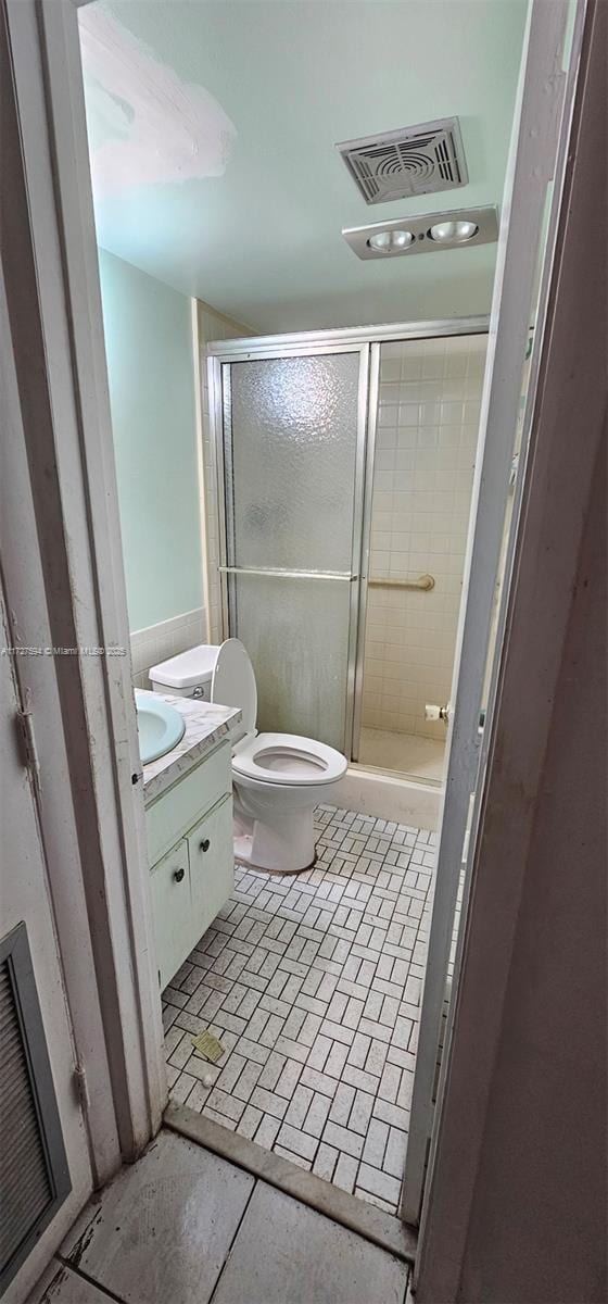 bathroom with an enclosed shower, vanity, toilet, and tile patterned flooring