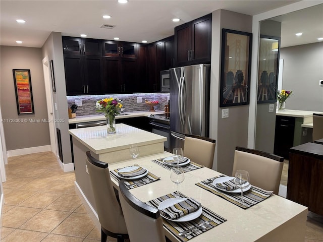 kitchen featuring dark brown cabinets, backsplash, light tile patterned floors, a center island, and stainless steel appliances