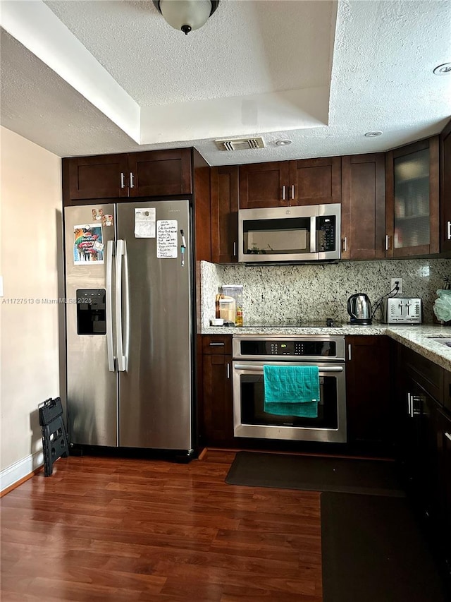 kitchen featuring light stone countertops, dark brown cabinets, appliances with stainless steel finishes, and dark wood-type flooring