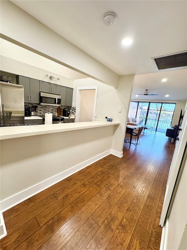 kitchen featuring appliances with stainless steel finishes, kitchen peninsula, backsplash, dark hardwood / wood-style floors, and gray cabinets