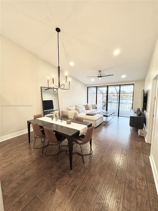 dining room with dark wood-type flooring, ceiling fan with notable chandelier, and a wall of windows