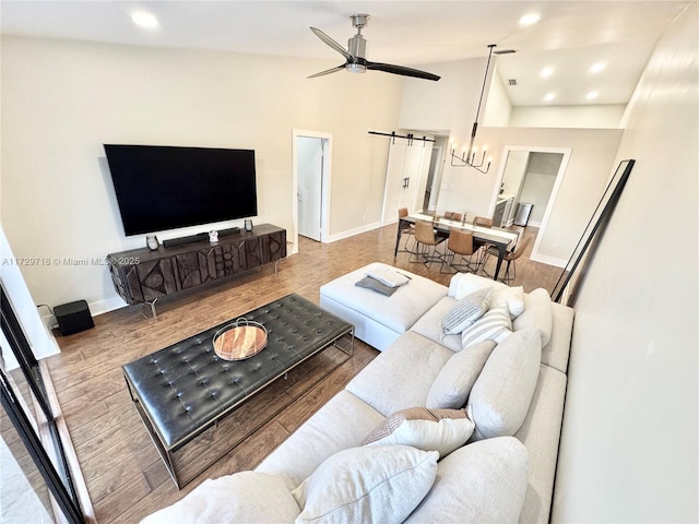 living room featuring light wood-type flooring, vaulted ceiling, ceiling fan, and a barn door