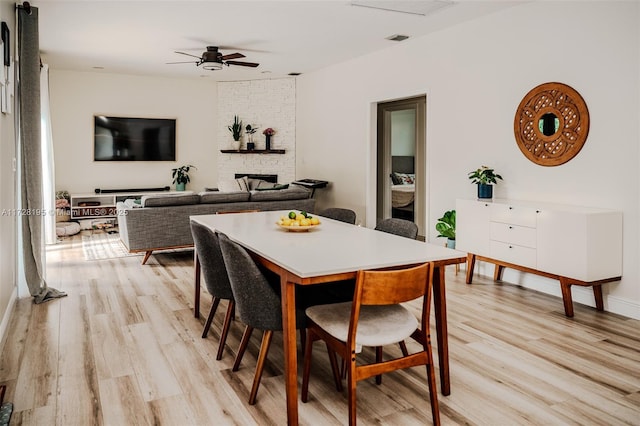 dining space featuring ceiling fan, a stone fireplace, and light hardwood / wood-style floors