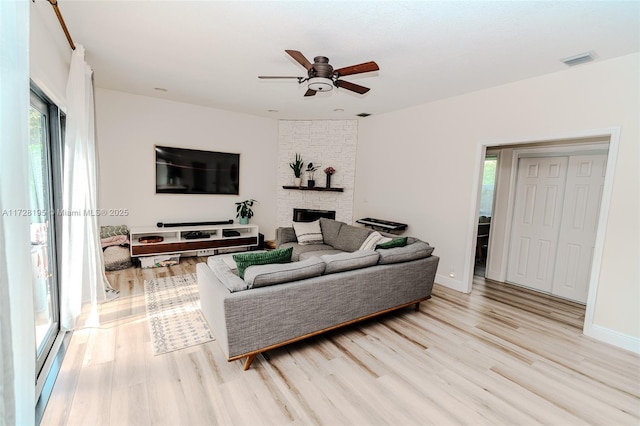 living room with light hardwood / wood-style floors, a healthy amount of sunlight, and a stone fireplace