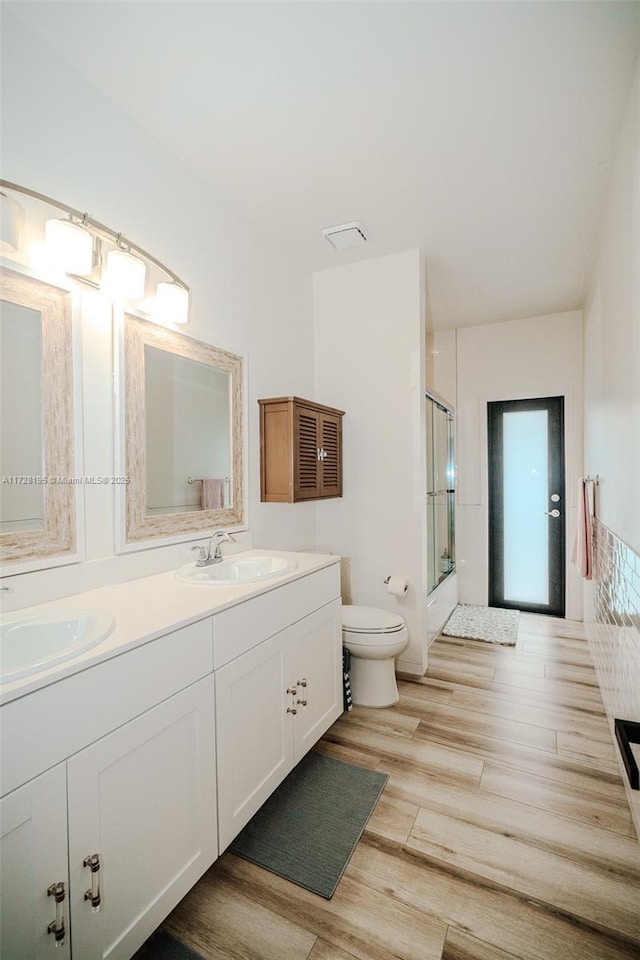 bathroom with wood-type flooring, a shower with door, toilet, and vanity