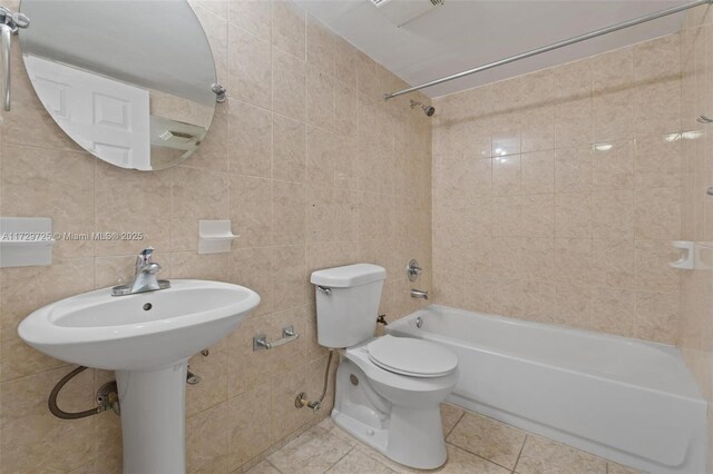 bathroom featuring tiled shower / bath, tile patterned floors, toilet, and tile walls