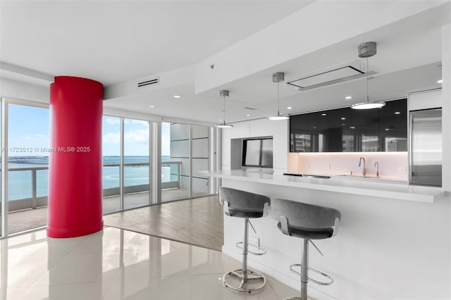 kitchen featuring a wall of windows, light tile patterned floors, built in refrigerator, decorative light fixtures, and sink