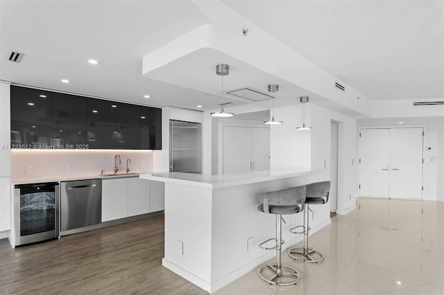 kitchen featuring white cabinetry, sink, pendant lighting, stainless steel appliances, and wine cooler