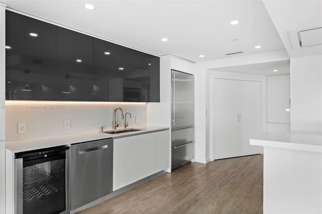 kitchen with appliances with stainless steel finishes, sink, light wood-type flooring, white cabinets, and beverage cooler