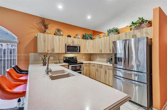 kitchen featuring kitchen peninsula, stainless steel appliances, light tile patterned flooring, light brown cabinetry, and sink