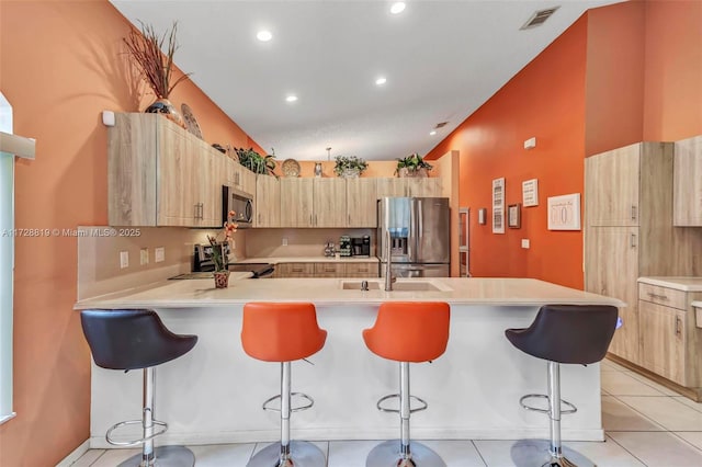 kitchen with kitchen peninsula, a kitchen bar, light brown cabinets, stainless steel appliances, and light tile patterned floors