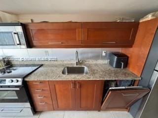 kitchen with light stone counters, sink, light tile patterned floors, and stainless steel appliances