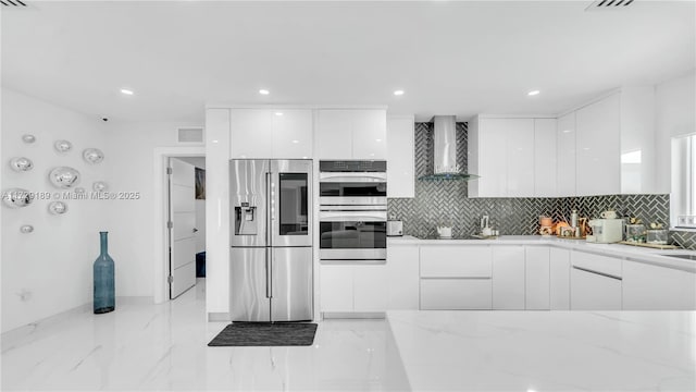 kitchen with backsplash, white cabinets, wall chimney range hood, and appliances with stainless steel finishes