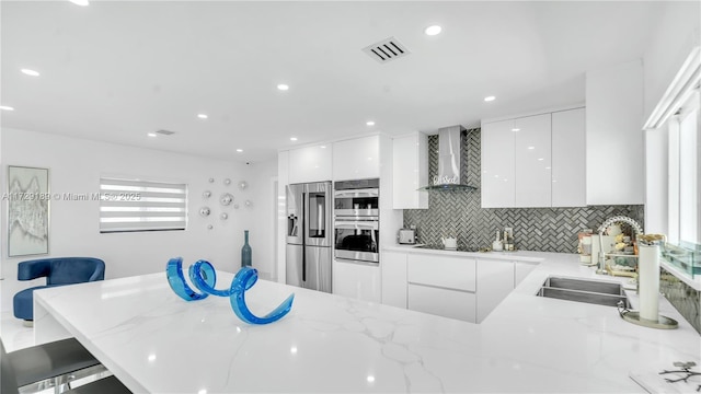 kitchen with wall chimney exhaust hood, white cabinetry, stainless steel appliances, a kitchen breakfast bar, and sink