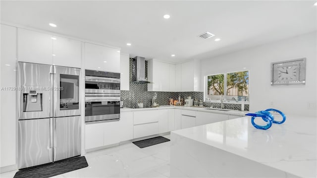 kitchen with backsplash, white cabinets, wall chimney range hood, and appliances with stainless steel finishes