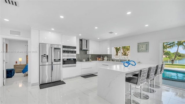 kitchen featuring a breakfast bar, white cabinetry, stainless steel appliances, and wall chimney exhaust hood