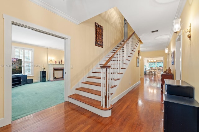 stairway featuring crown molding, an inviting chandelier, and wood-type flooring