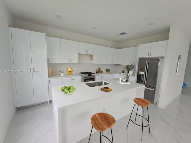 kitchen featuring white cabinets, fridge with ice dispenser, a kitchen island with sink, and stainless steel range with gas stovetop