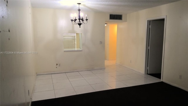 tiled empty room with a textured ceiling and a chandelier