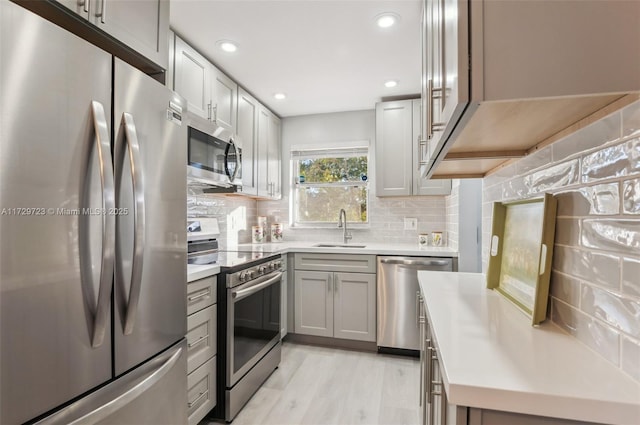 kitchen featuring stainless steel appliances, light hardwood / wood-style floors, sink, decorative backsplash, and gray cabinets