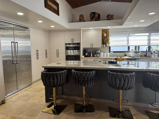 kitchen featuring appliances with stainless steel finishes, sink, white cabinets, light stone countertops, and a kitchen bar