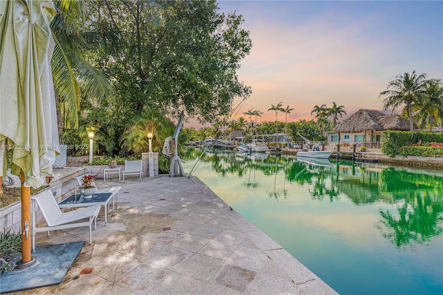 patio terrace at dusk featuring a water view and a boat dock