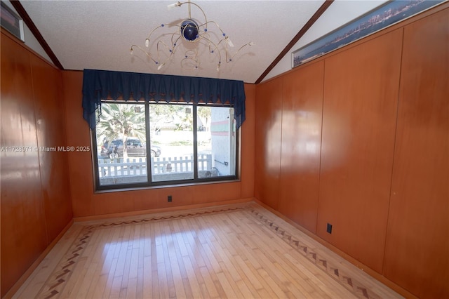 unfurnished room featuring a textured ceiling, light hardwood / wood-style flooring, wood walls, and vaulted ceiling