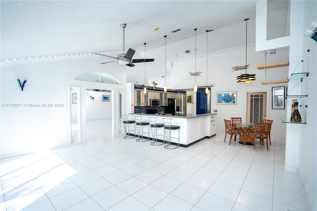 kitchen featuring decorative light fixtures, light tile patterned floors, high vaulted ceiling, decorative backsplash, and stainless steel appliances